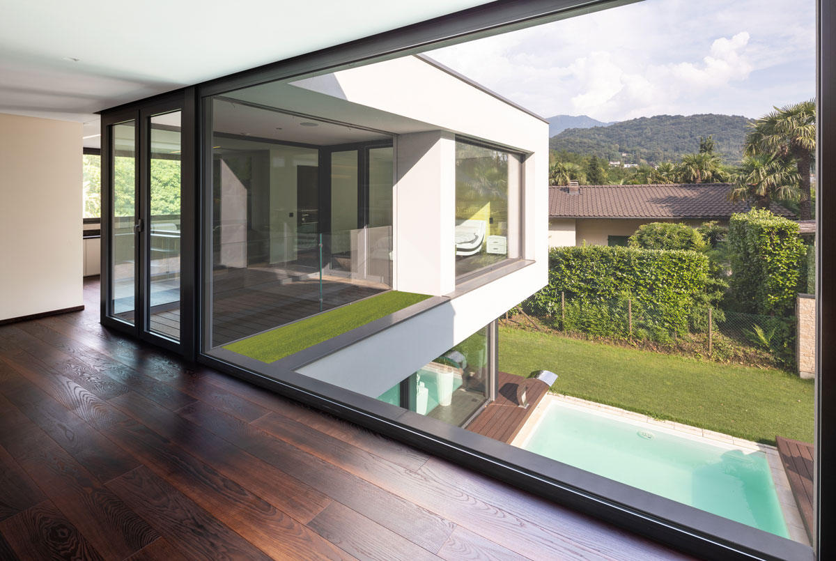 Vista desde el interior de una casa moderna con amplios cerramientos de vidrio laminado, mostrando el exterior con jardín y piscina