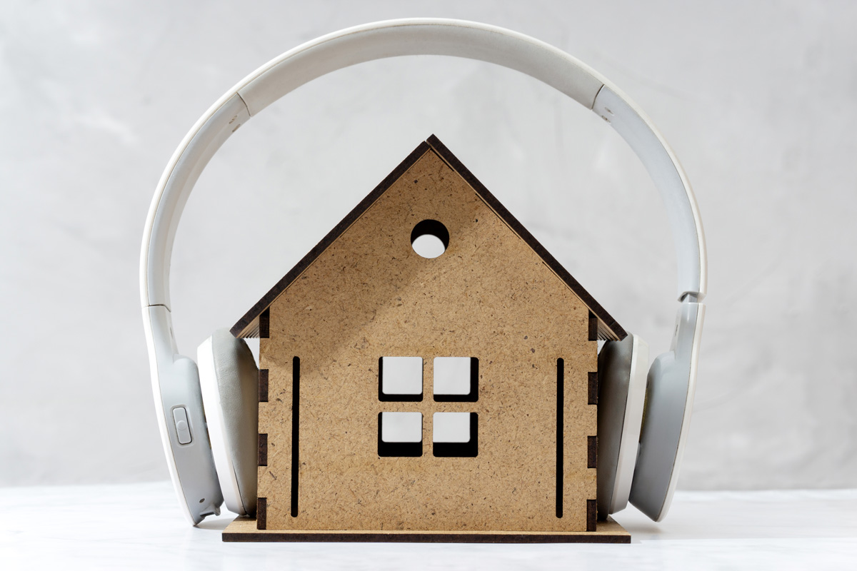 Una maqueta de casa con auriculares puestos, simbolizando la reducción de ruido y el aislamiento acústico en el hogar.