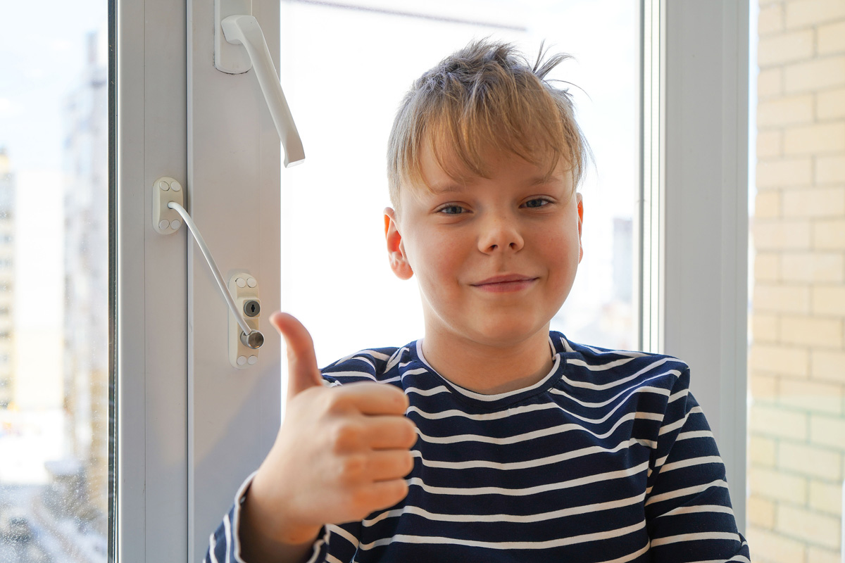 Niño mostrando gesto de aprobación junto a ventana con dispositivo de seguridad infantil