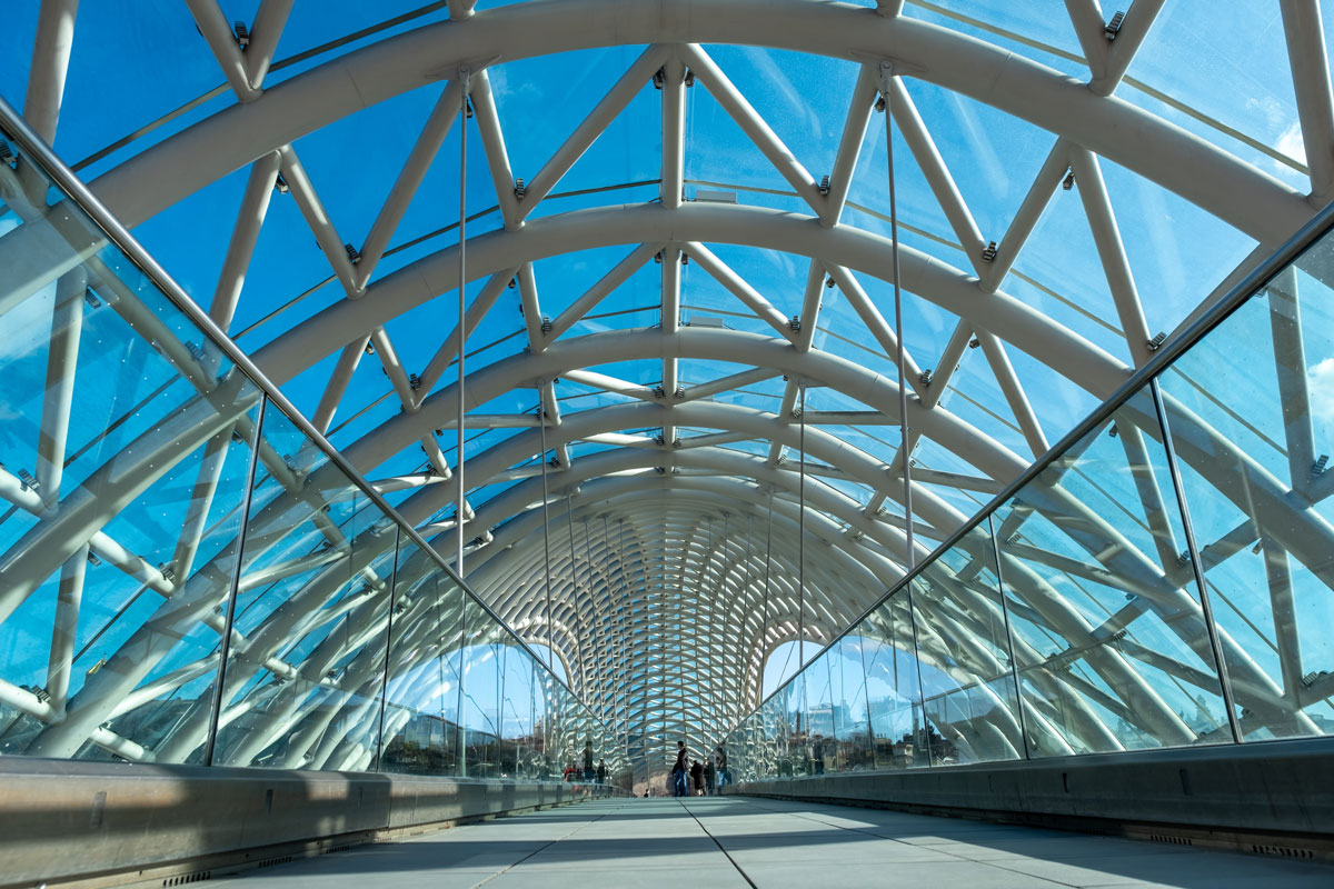 Pasarela cubierta con vidrio curvado y estructura moderna, con barandillas de cristal