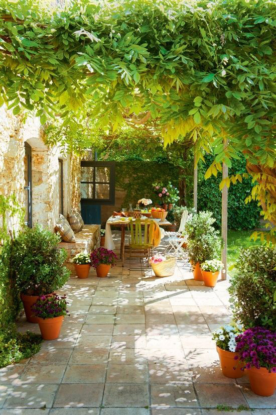 Terraza rústica con sombra vegetal natural, plantas en macetas y zona de comedor exterior.