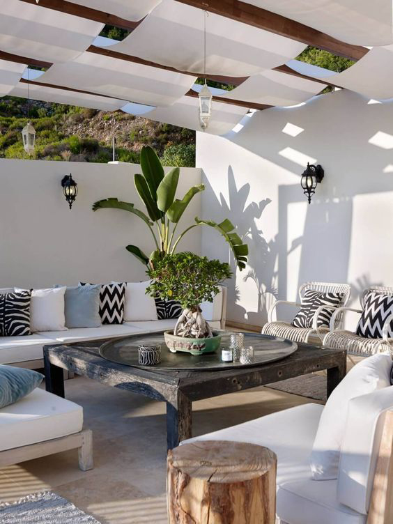 Terraza mediterránea con sombra de lonas y sofá blanco en L