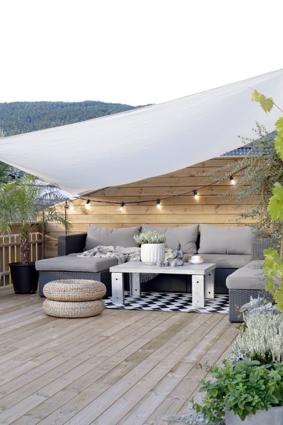 Espacio chill out con sofá en L y toldo blanco en terraza de madera