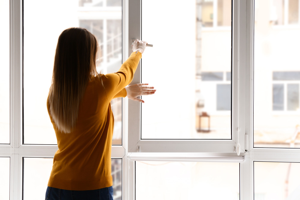 Mujer abriendo ventana abatible oscilobatiente de PVC con cierre hermético