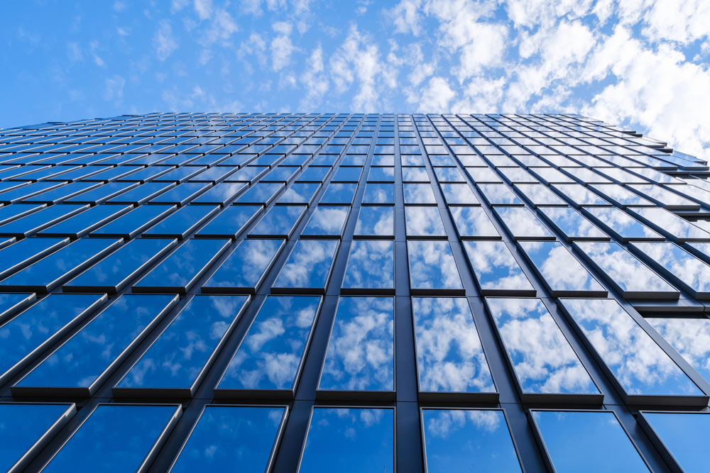 Fachada acristalada moderna con reflejos de cielo, símbolo de eficiencia energética y diseño sostenible.